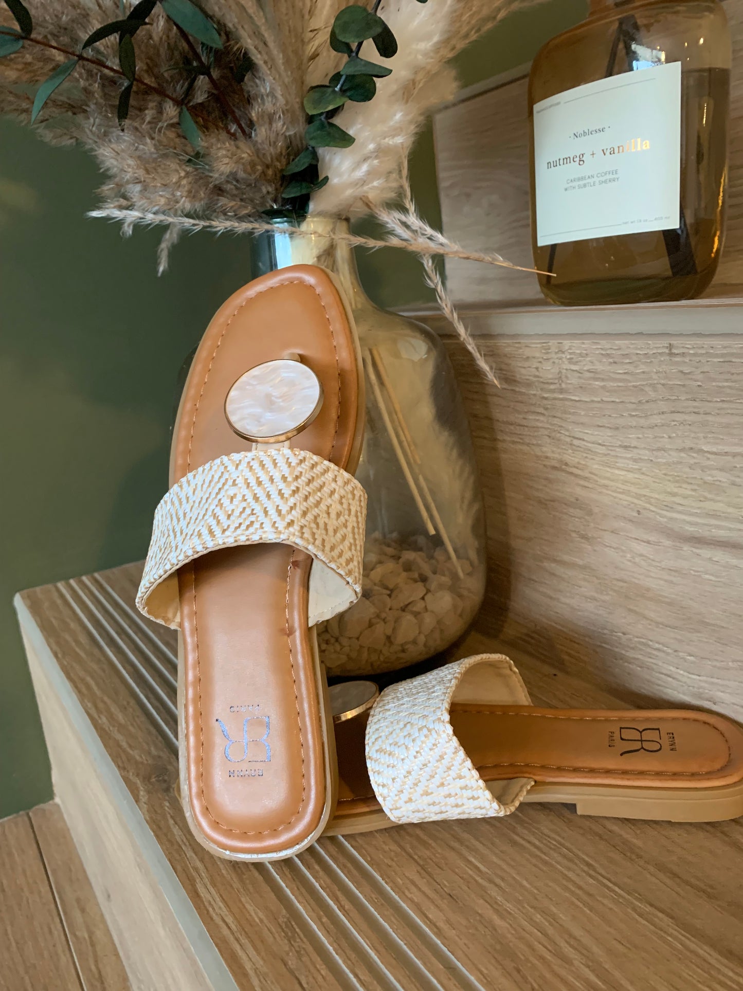 Sandales plates Luna Chic avec anneau nacré et bande tressée beige, vue de dessus posées sur étagère bois clair en ambiance naturelle chic