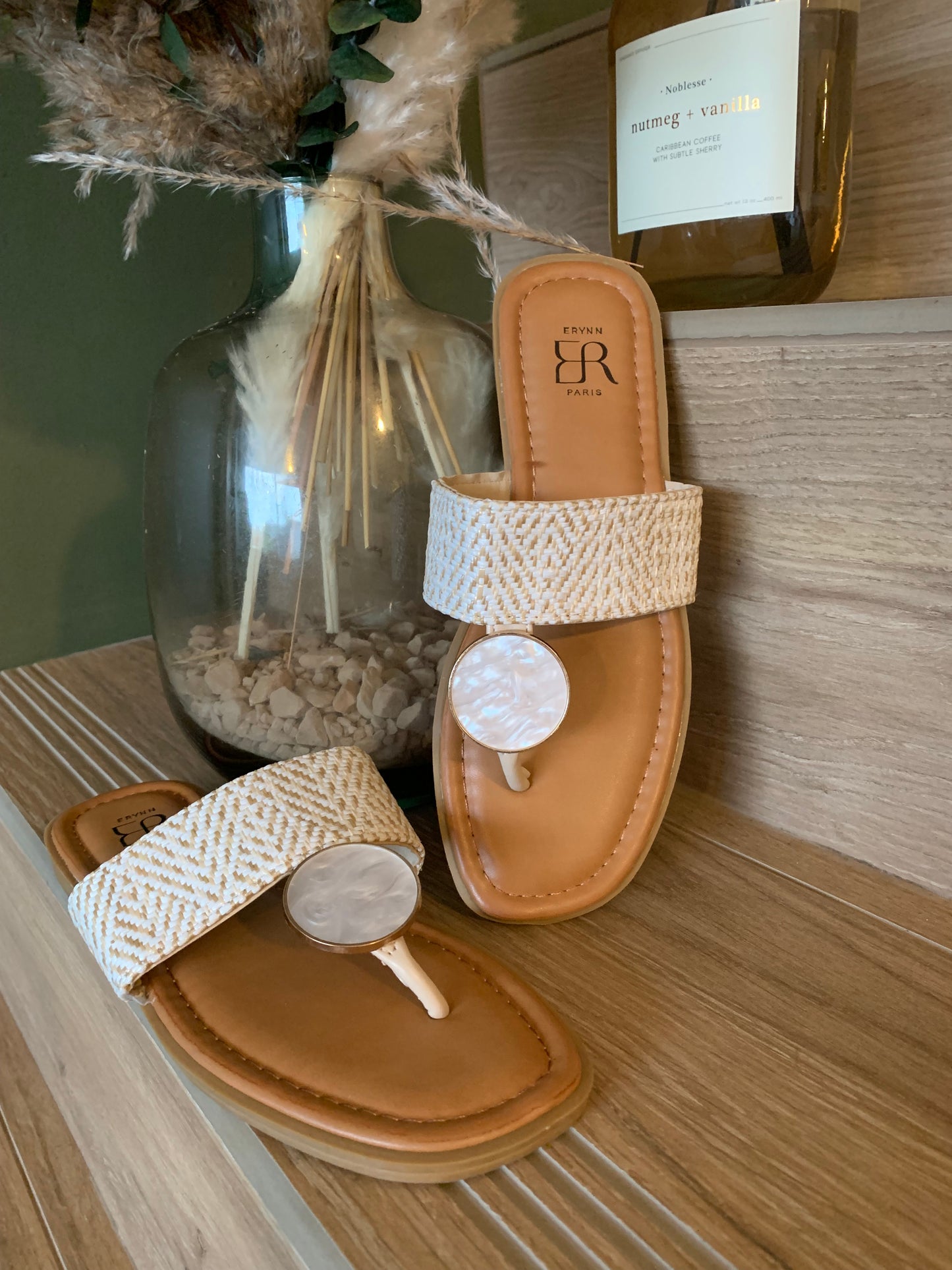 Sandales plates Luna Chic avec anneau nacré et large bande tissée beige, présentées en duo sur fond bois naturel avec décoration végétale